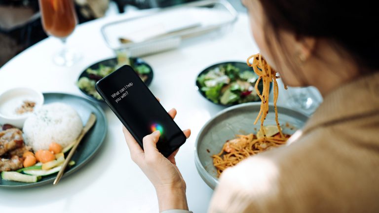 Sprachassistenten Eine Person hält ein iPhone in der Hand. Darauf ist Siri zu erkennen, die auf ein Kommando wartet.