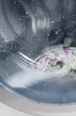 Blick in eine Waschtrommel. Darin sind Wasser und Kleidungsstücke zu sehen.