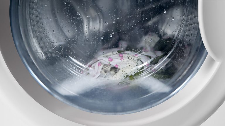 Blick in eine Waschtrommel. Darin sind Wasser und Kleidungsstücke zu sehen.