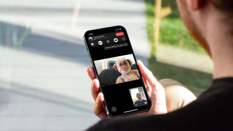 Eine Person hält ein iPhone in der Hand. Auf dem Bildschirm ist ein laufendes FaceTime-Gespräch zu sehen.
