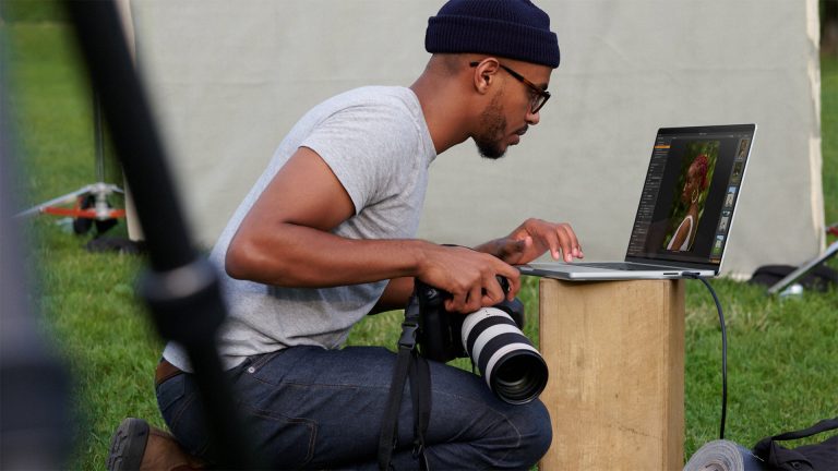Eine Person mit einer Kamera in der Hand betrachtet die geschossenen Bilder auf einem MacBook Pro.