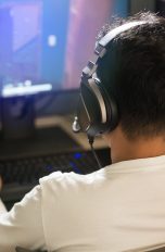 Eine Person mit einem Headset auf dem Kopf sitzt vor einem Rechner und spielt etwas.