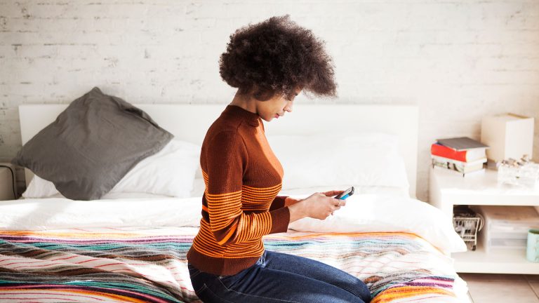 Gelöschte Fotos wieder herstellen bei Android Eine Person sitzt auf dem Bett und hält ein Smartphone in den Händen.