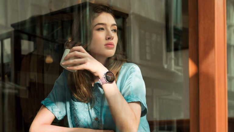 Eine Person sitzt in einem Café und schaut aus dem Fenster. An ihrem Handgelenk ist eine Huawei Watch GT 3 zu sehen.