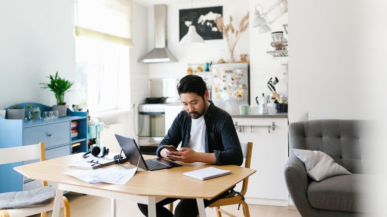Eine Person sitzt an einem Tisch mit einem Laptop vor sich und arbeitet.