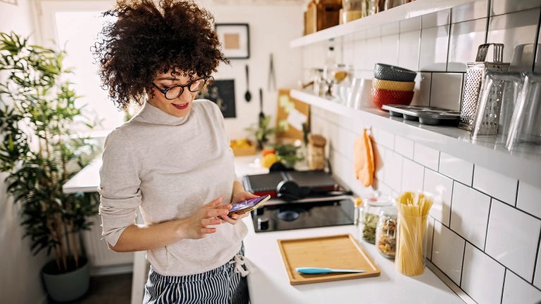Mesh-WLAN Eine Person steht in der Küche und schaut auf das Smartphone in ihrer Hand.
