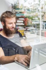 Eine Person sitzt an einem Laptop und tippt. Im Hintergrund sind Bücherregale zu sehen.
