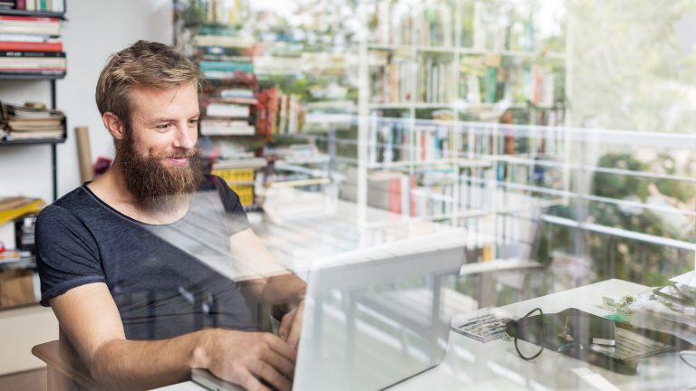 Eine Person sitzt an einem Laptop und tippt. Im Hintergrund sind Bücherregale zu sehen.
