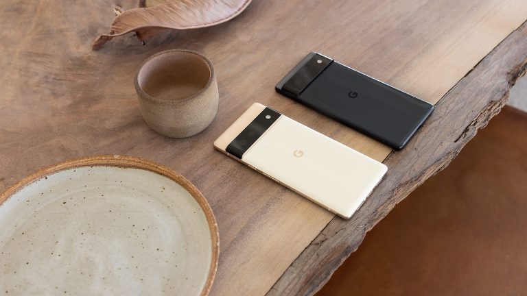 Google Pixel 6 und Pixel 6 Pro Ein Pixel 6 liegt neben einem Pixel 6 Pro mit dem Display nach unten auf einem Holztisch.