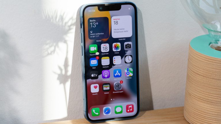 Display-Technologien Ein iPhone 13 Mini steht, gegen eine Wand gelehnt, auf einem Sideboard.