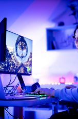 Eine Person spielt an einem Tisch, auf dem ein Laptop und zwei Monitore stehen.