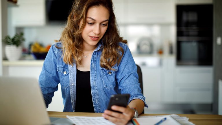 Google-Konto erstellen, ändern, löschen Eine Person sitzt vor einem Laptop und schaut auf ihr Smartphone.