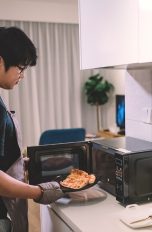Ein Person stellt ein Stück Pizza in eine Mikrowelle.
