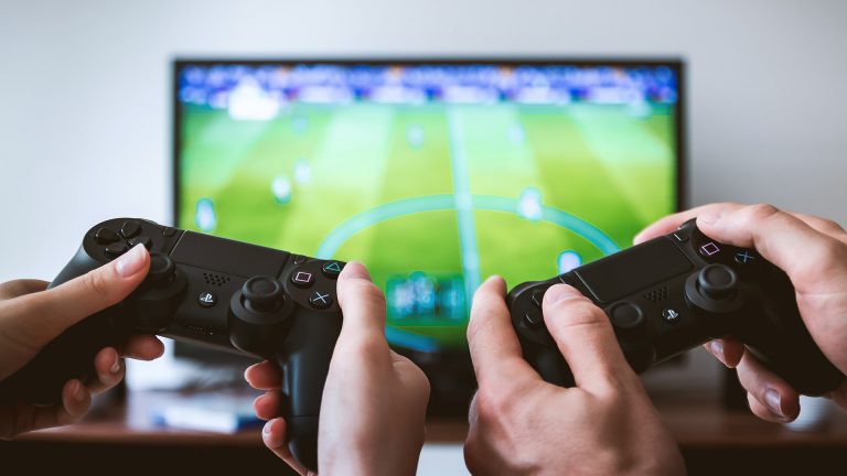 PS4-Controller verbindet sich nicht Zwei Paar Hände halten zwei PS4-Controller fest. Im Hintergrund ist ein Fernseher zu erkennen, auf dem ein FIFA-Spiel läuft.