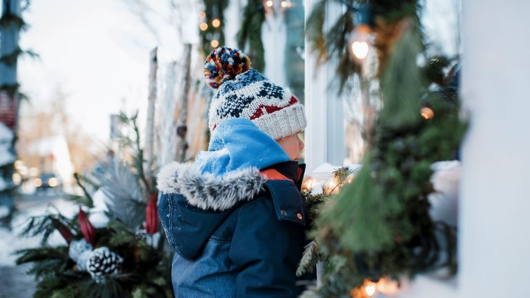 Weihnachtsbeleuchtung Ein Kind schaut durch ein Fenster in ein weihnachtlich geschmücktes Gebäude.