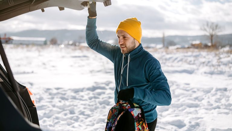 Der Winter naht Eine Person schaut in den geöffneten Kofferraum eines Autos. In der Hand hält sie einen bunten Rucksack.