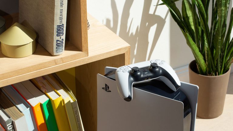 Playstation 5 Eine PlayStation 5 steht vor einem Bücherregal. Auf der Konsole liegt ein DualSense-Controller.