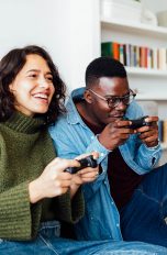Zwei Personen hocken vor einem Sofa. Beide halten einen PlayStation-4-Controller in den Händen.
