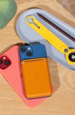 Ein iPhone 13 und ein 13 mini liegen auf einem Tisch. In einer Schale liegt ein Apple AirTag in einem gelben Rucksackanhänger.