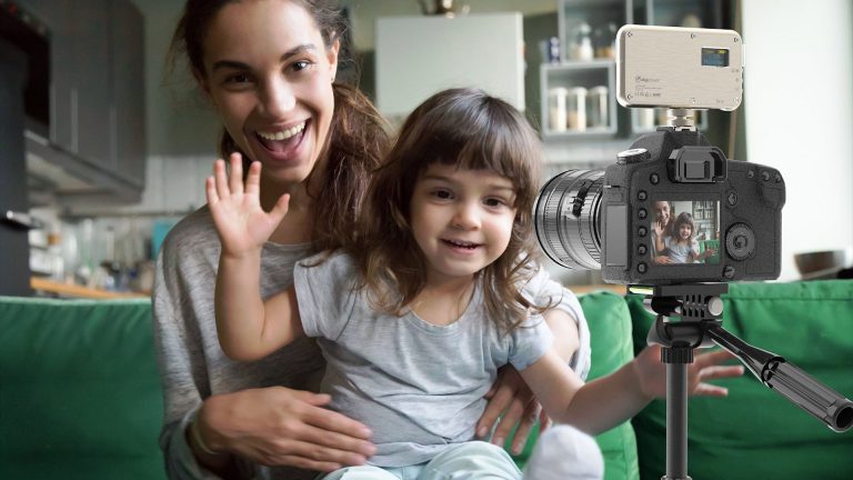 DigiPower Videoleuchte Eine Person hat ein Kind auf dem Schoss. Die beiden lächeln in eine Kamera, die vor ihnen steht.
