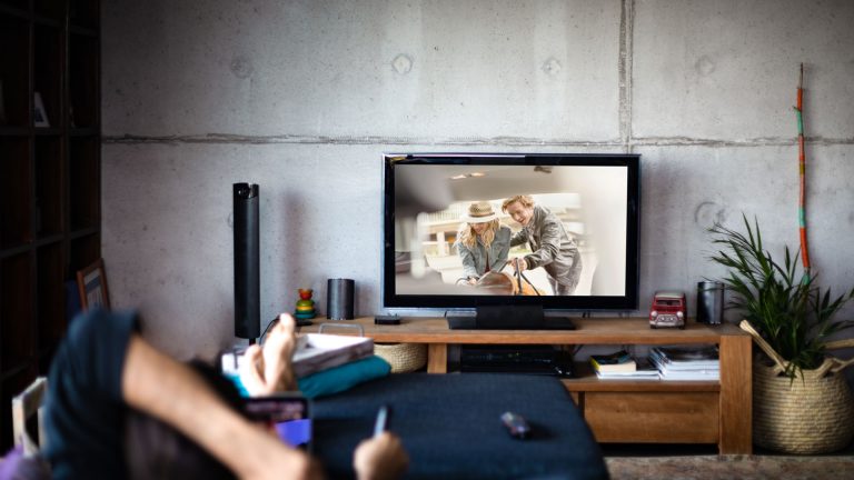 HbbTV Eine Person liegt auf dem Sofa und schaut etwas im TV an.