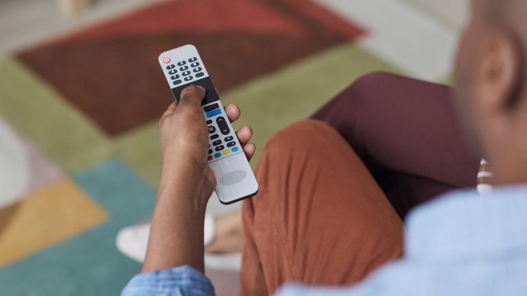 HbbTV Eine Person hält eine Fernbedienung in der Hand. Darauf ist auch der rote Knopf zu sehen.