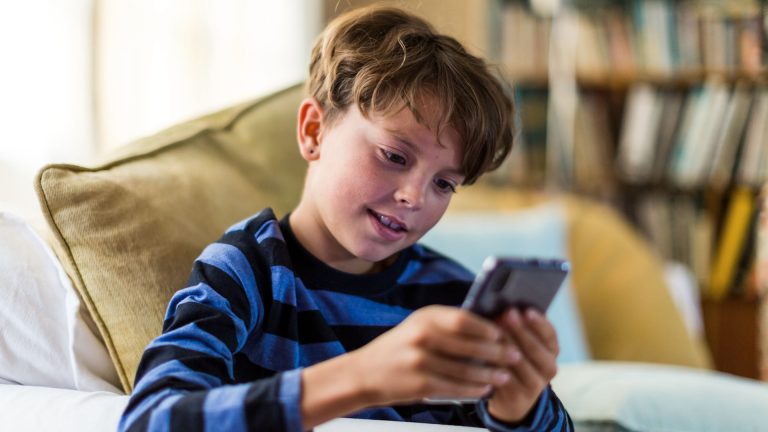 Smartphones für Kinder Ein Kind sitzt auf einem Sofa und spielt dabei auf einem Smartphone.