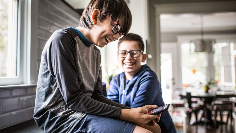 Smartphones für Kinder Zwei Kinder sitzen in einer Küche auf einer Arbeitsplatte und beschäftigen sich mit einem Smartphone.