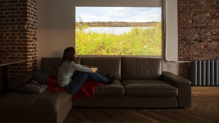 Eine Person sitzt auf einem Sofa vor der Projektion eines Beamers.