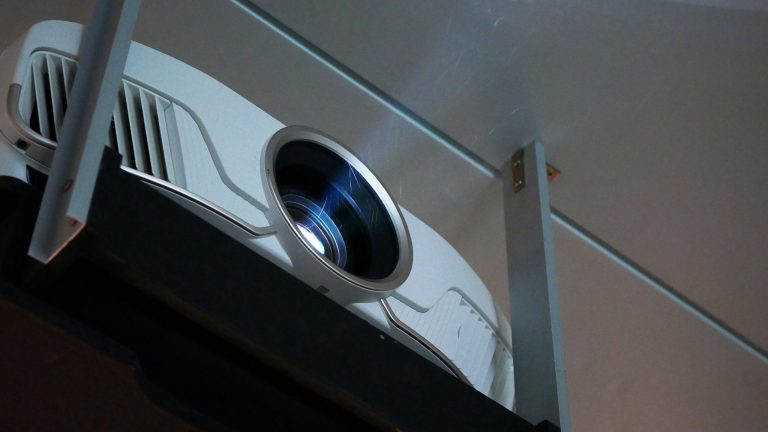Beamer installieren Nahaufnahme eines laufenden Beamers, dessen Lichtstrahl dezent zu sehen ist.
