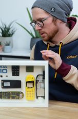 Nokia 5110 Bilderrahmen Eine Person steht hinter einem selbstgebauten Technik-Bilderrahmen. Darin befindet sich ein in seine Einzelteile zerlegtes Nokia 5110.