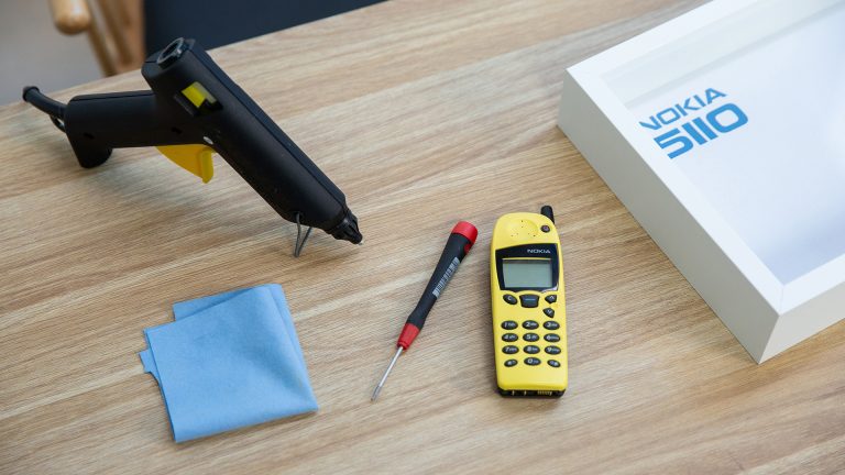 Nokia 5110 Bilderrahmen Auf einem Tisch liegen Arbeitsmaterialien für einen Technik-Bilderrahmen: ein Nokia 5110, ein Torx-Schraubendreher, eine Heißklebepistole, ein Putztuch und ein Objektrahmen.