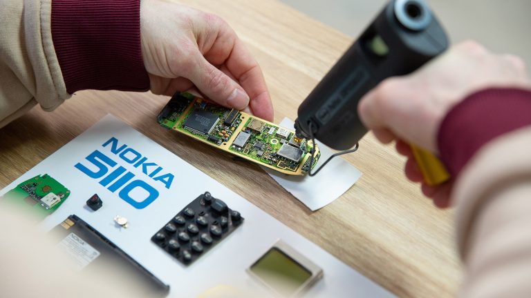Nokia 5110 Bilderrahmen Eine Person verteilt Kleber mithilfe einer Heizklebepistole auf der Platine eines Nokia 5110.