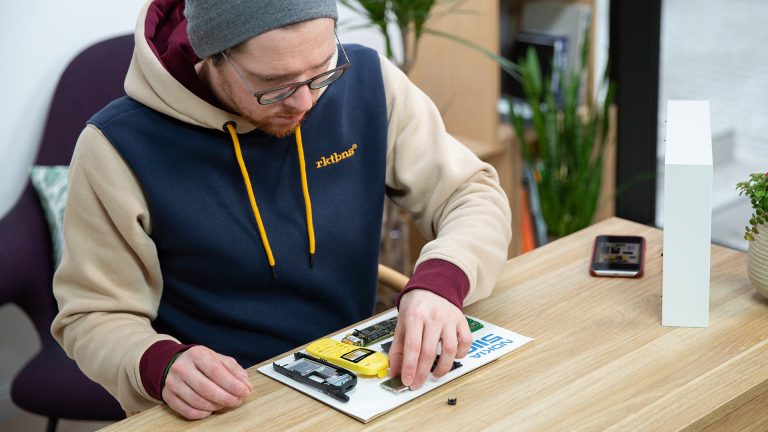 Nokia 5110 Bilderrahmen Eine Person legt die verklebten Bauteile auf ein DIN-A4-Blatt, um sie dort zu fixieren.