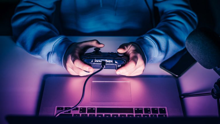 Eine Person spielt mit einem Controller ein Spiel auf einem MacBook.
