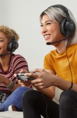 Zwei Personen sitzen auf dem Sofa, spielen auf einer PS4 und tragen dabei das Headset JBL Quantum.