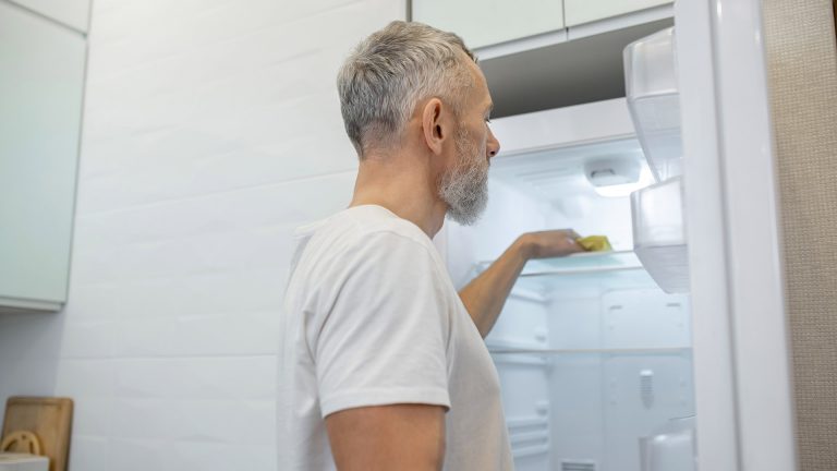 Wasser im Kühlschrank Eine Person wischt einen leeren Kühlschrank mit einem Lappen aus.
