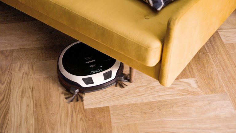 Miele Saugroboter Scout RX3 Ein Saugroboter guckt unter einem Sofa hervor.