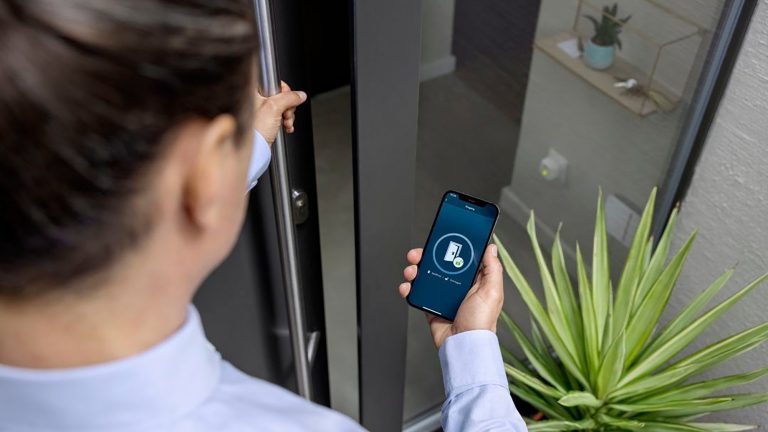 Bosch Yale Linus Smart Lock Eine Person steht an ihrer Haustür und blickt auf die zu ihrem smarten Schloss gehörende App.