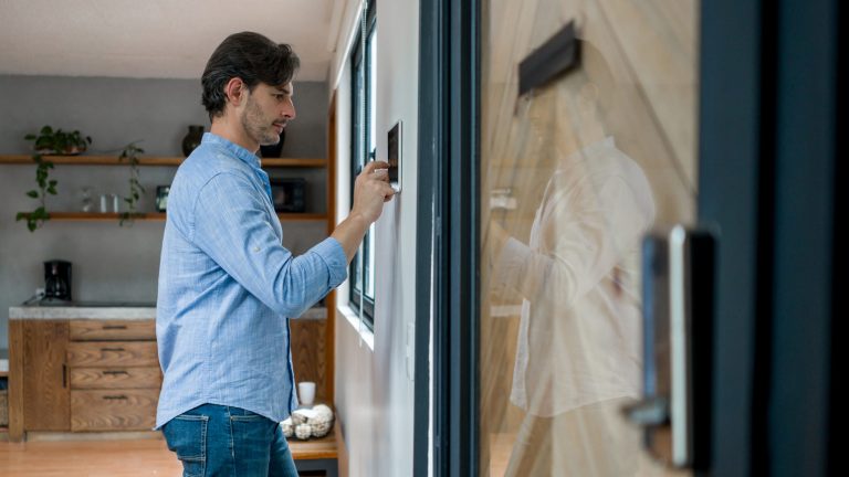 Smart Lock Ein Mann steht vor einer Wand, an der ein Display hängt, über das er seine Smart Home-Geräte programmiert.