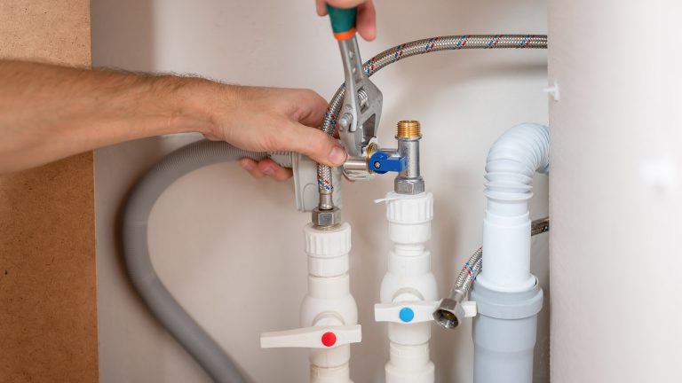 Spülmaschine zieht kein Wasser Zwei Hände befestigen Zu- und Ablaufschlauch einer Spülmaschine.