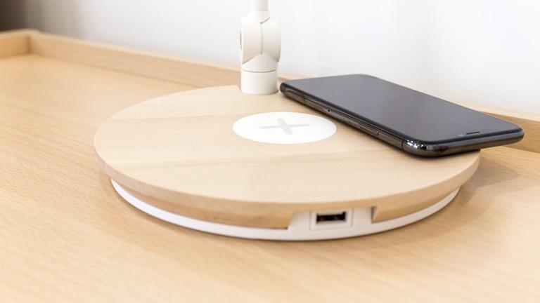 induktives Laden Ein Smartphone liegt auf dem Fuß einer Tischlampe, in dem eine Ladestation untergebracht ist.