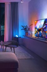 Eine Person sitzt vor einem Fernseher, an dessen Rückseite Hue Play Gradient angebracht ist.