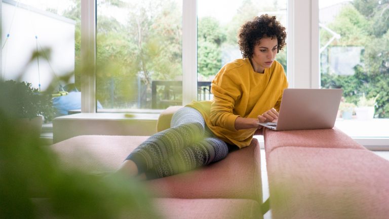 Festplatte an Fritzbox anschließen Eine Person liegt auf dem Sofa und bedient ihren Laptop.