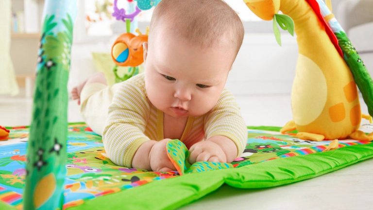 Fisher-Price Erlebnisdecke Regenwald Ein Baby liegt auf dem Bauch auf einer Spieldecke und spielt.