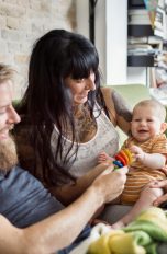Eltern und ihr kleines Baby sitzen zusammen auf einem Sofa.