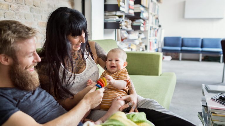 Eltern und ihr kleines Baby sitzen zusammen auf einem Sofa.