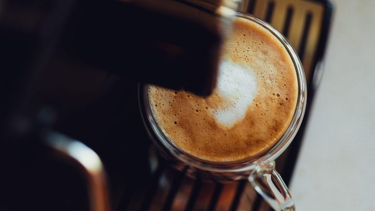 Kaffeevollautomaten Unter dem Kaffeeauslauf eines Kaffeevollautomaten steht eine Kaffeetasse gefüllt mit Kaffee und Milchschaum.