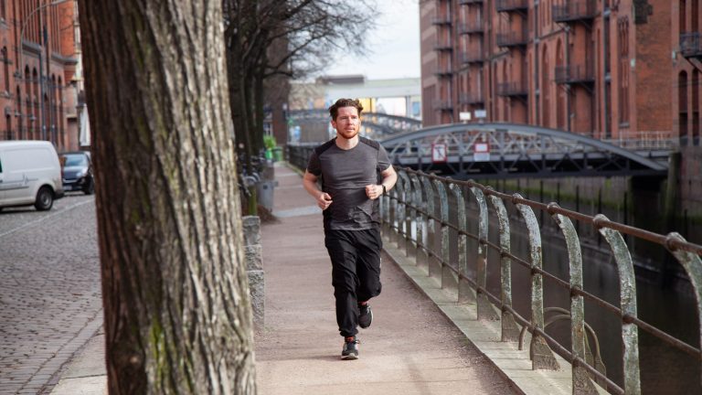 Eine Person läuft in der Speicherstadt in Hamburg an der Straße entlang und trägt dabei einen Fitnesstracker.