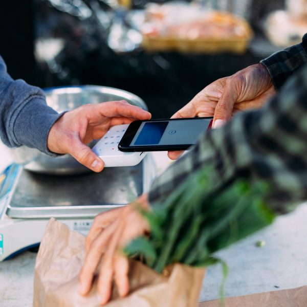 Eine Person zahlt mit einem Smartphone an einem Marktstand.